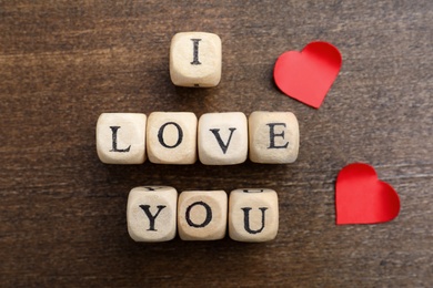 Photo of Cubes with words I Love You and paper hearts on wooden background, flat lay