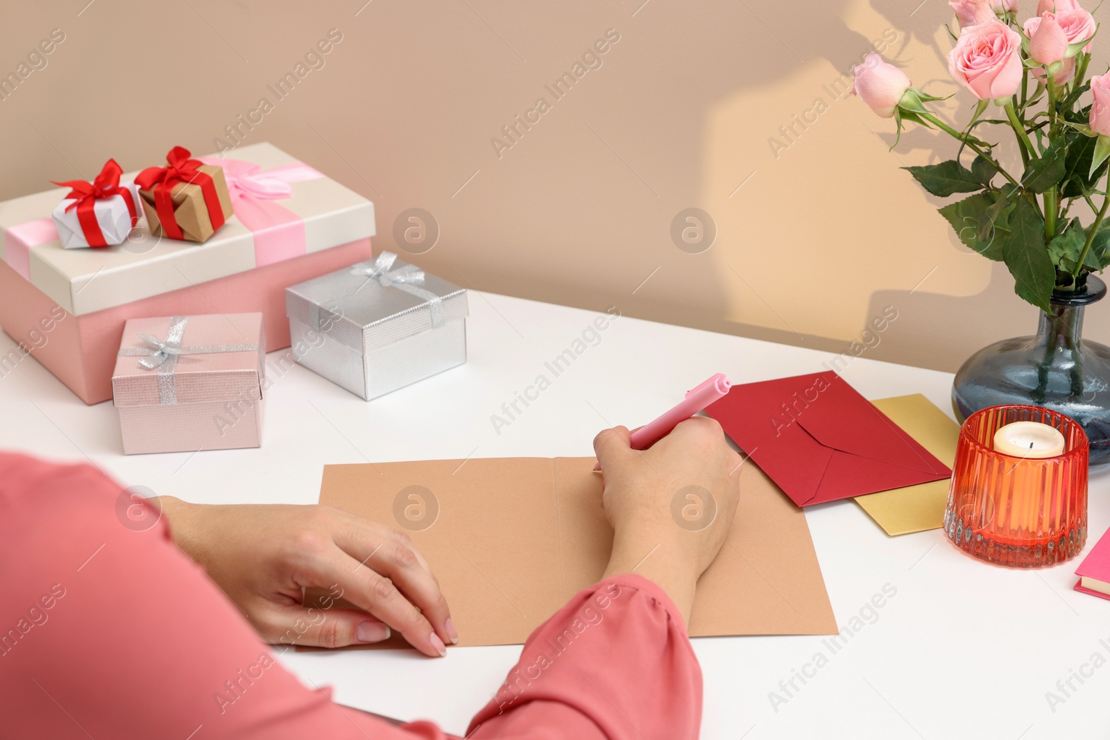 Photo of Young woman writing message in greeting card at white table, closeup