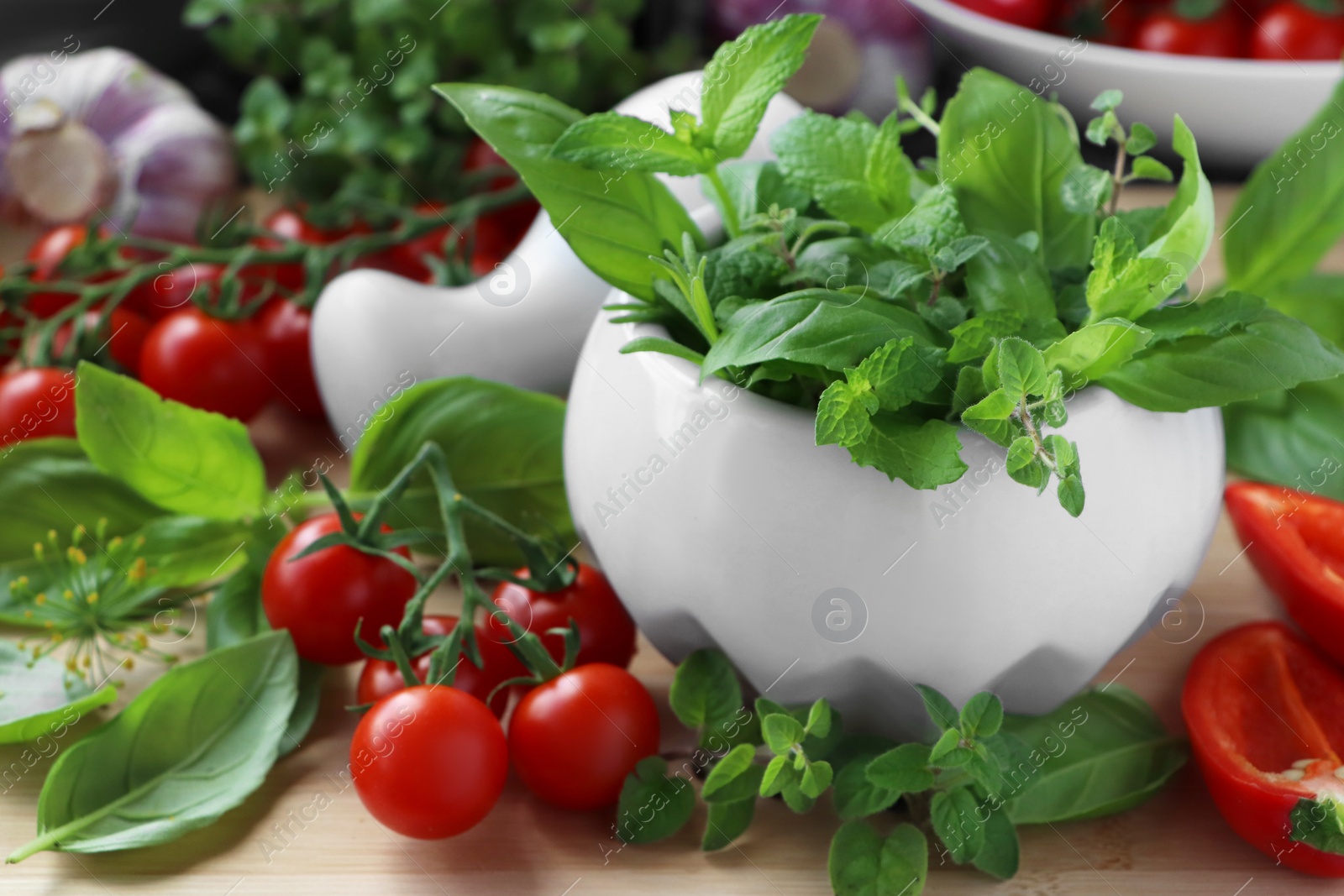 Photo of Mortar with fresh herbs, pepper and cherry tomatoes on wooden table, closeup