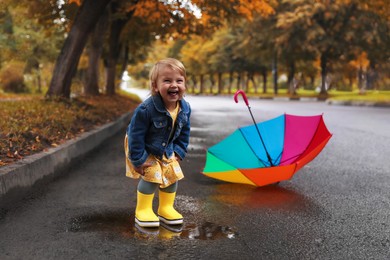 Cute little girl standing in puddle near colorful umbrella outdoors