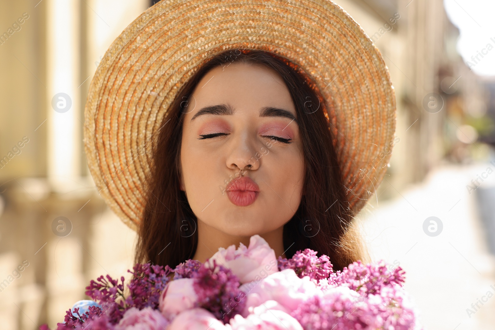 Photo of Beautiful woman with bouquet of spring flowers sending air kiss outdoors