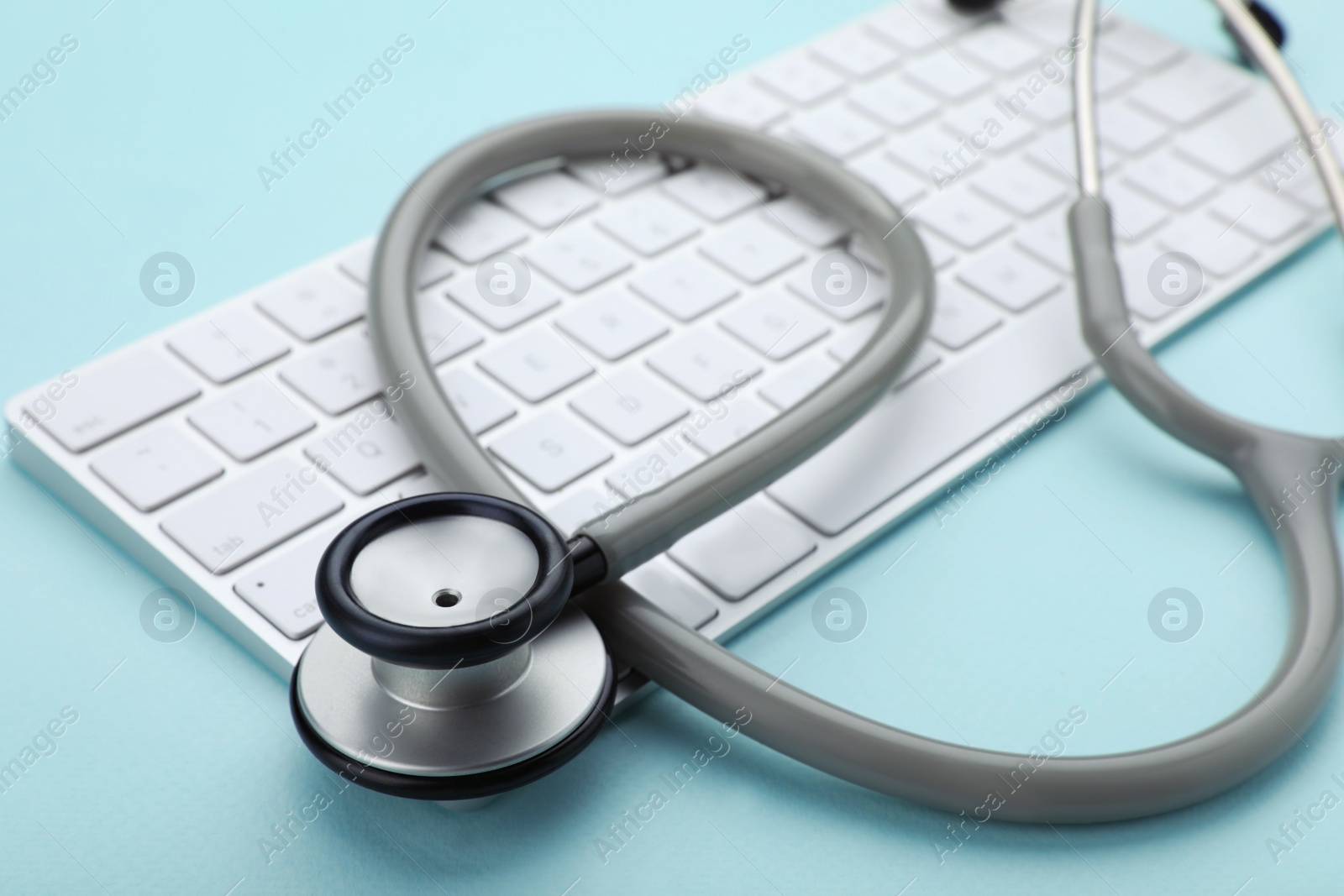 Photo of Computer keyboard with stethoscope on turquoise background, closeup