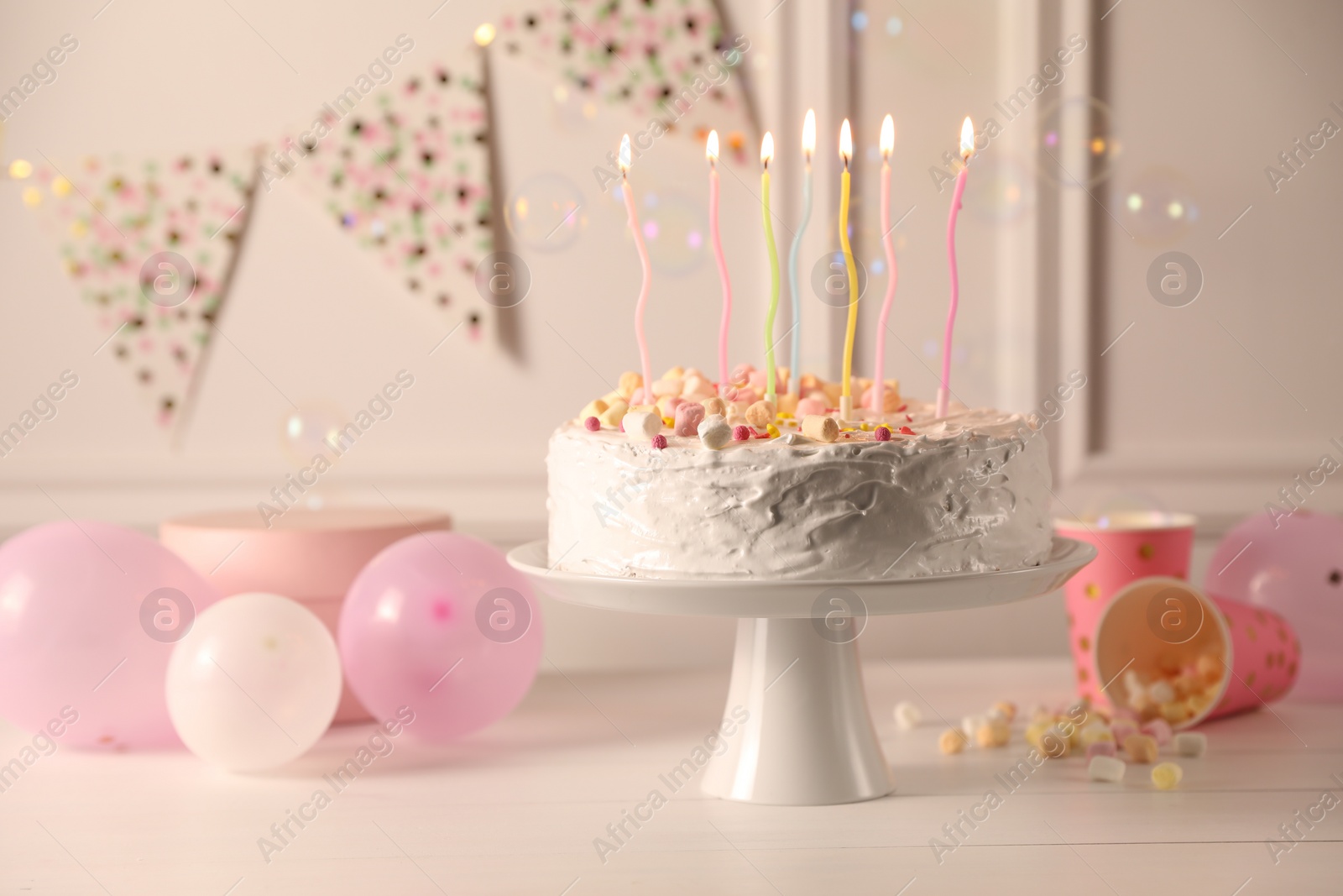 Photo of Tasty Birthday cake with burning candles and party decor on white table