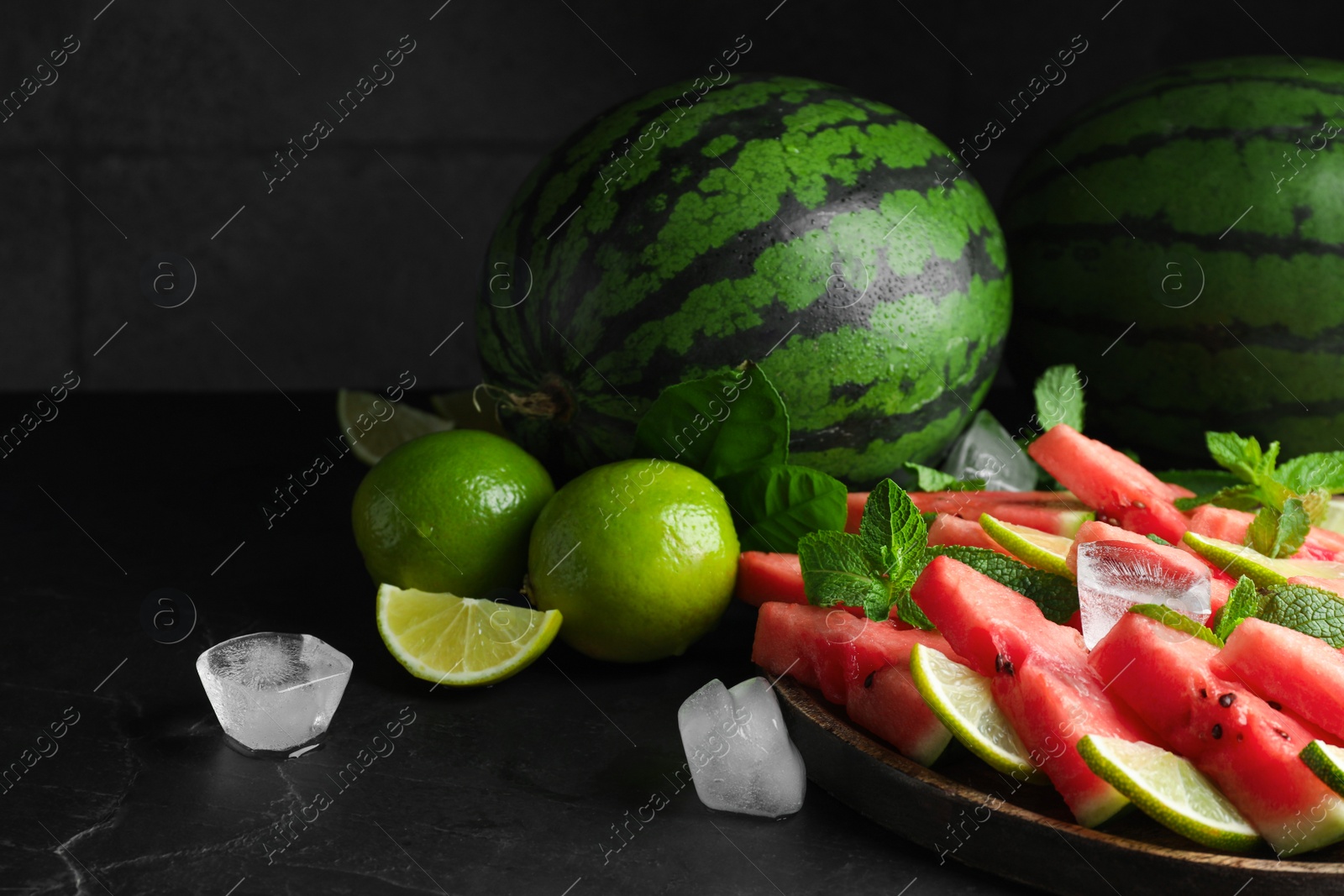 Photo of Tasty sliced watermelon, limes, mint and ice on black table