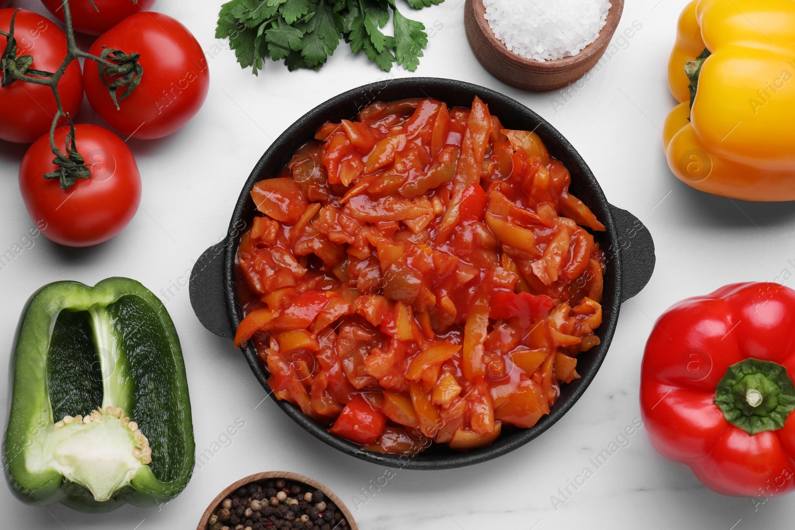 Photo of Delicious lecho in frying pan and ingredients on white table, flat lay