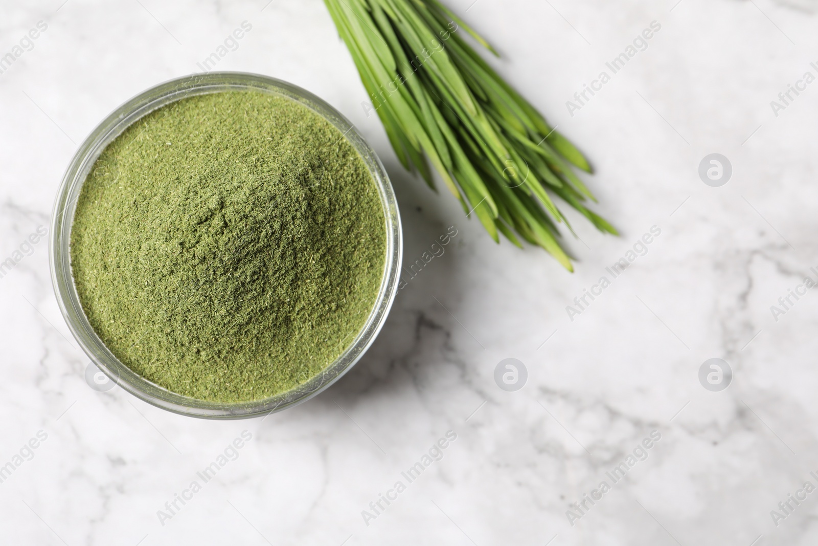 Photo of Wheat grass powder in bowl and fresh sprouts on white marble table, flat lay. Space for text