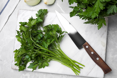 Photo of Marble board with fresh green parsley and knife on grey table, flat lay