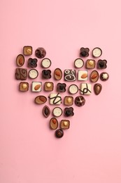 Heart made with delicious chocolate candies on pink background, top view