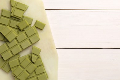 Pieces of tasty matcha chocolate bars on white wooden table, top view. Space for text