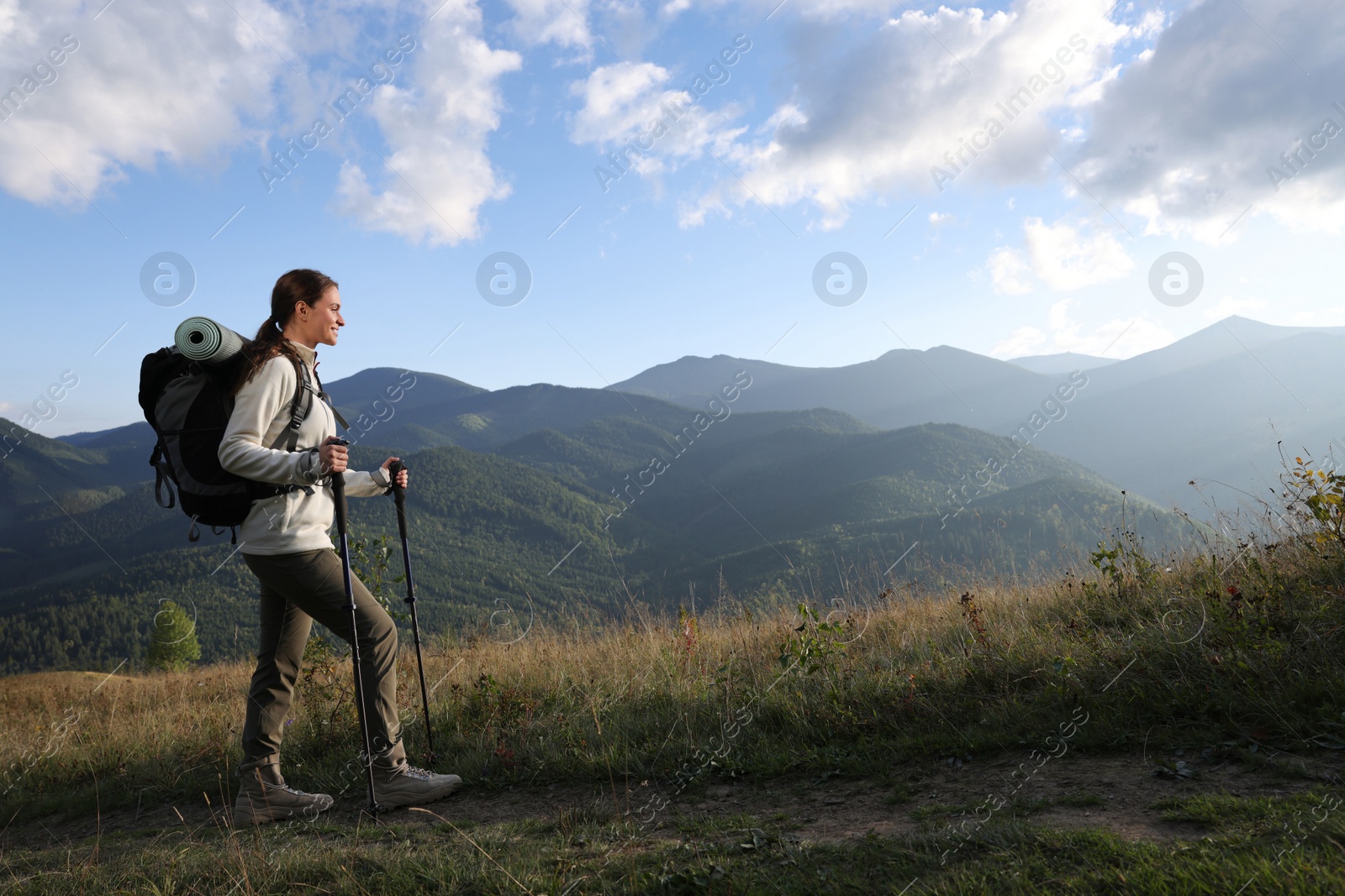 Photo of Tourist with backpack and trekking poles hiking through mountains, space for text