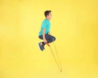 Active boy jumping rope on color background
