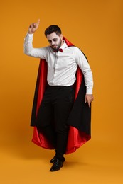 Photo of Man in scary vampire costume with fangs posing on orange background. Halloween celebration