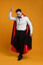 Man in scary vampire costume with fangs posing on orange background. Halloween celebration