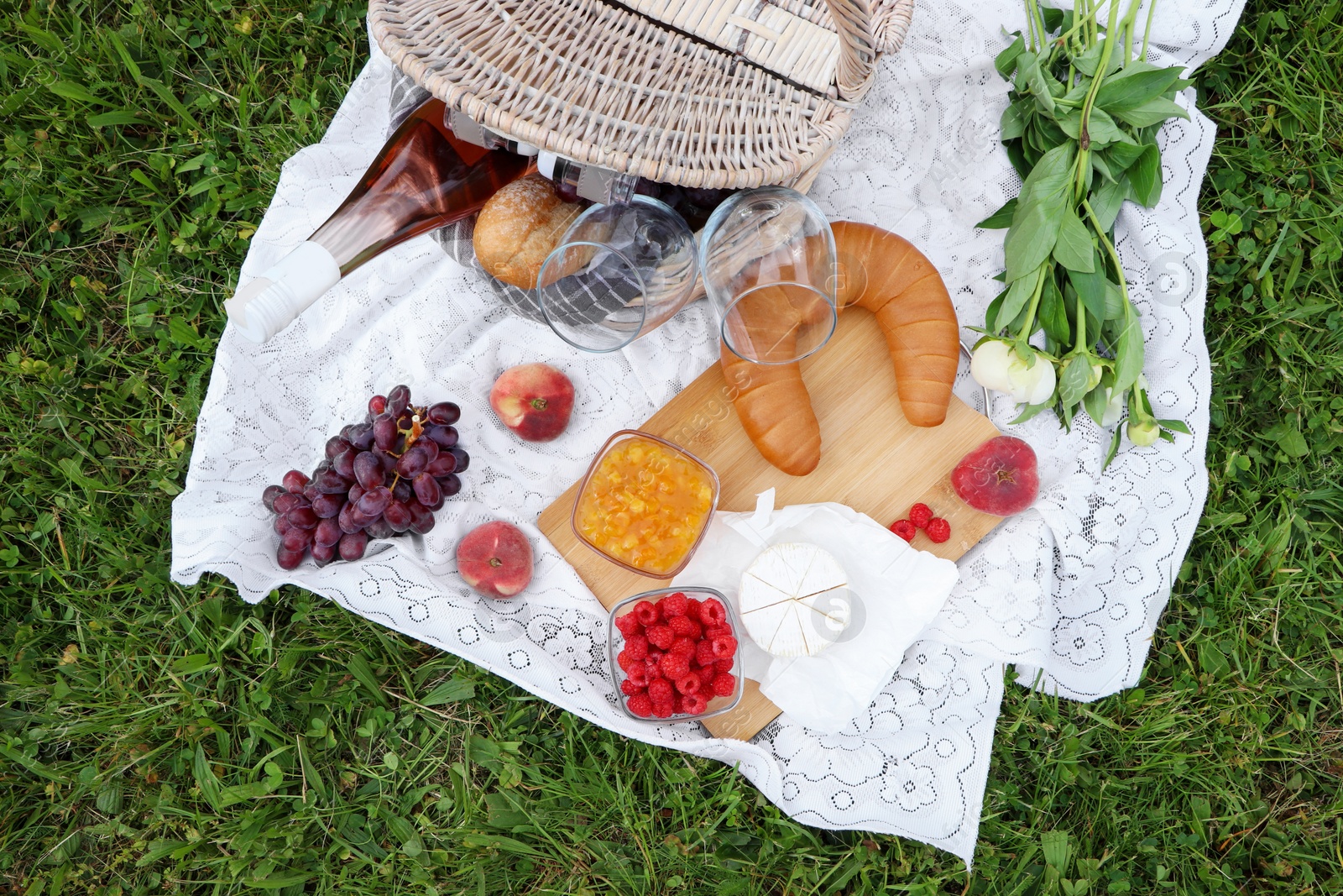 Photo of Picnic blanket with tasty food, flowers and cider on grass outdoors, flat lay