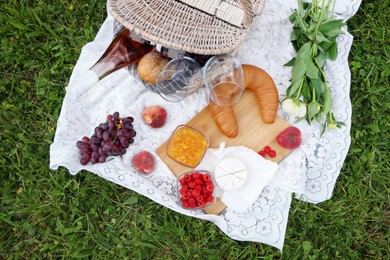 Picnic blanket with tasty food, flowers and cider on grass outdoors, flat lay