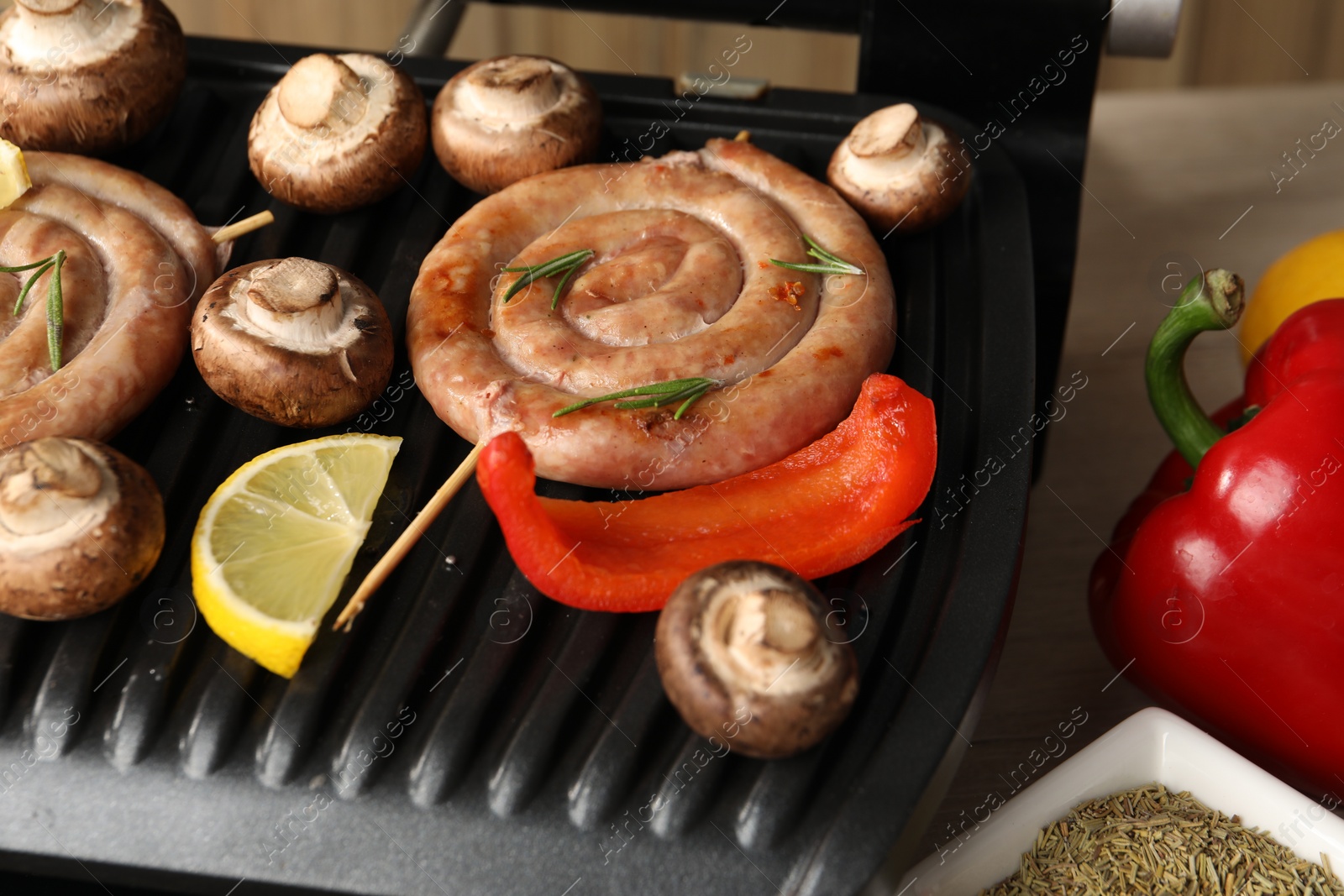 Photo of Electric grill with homemade sausages, mushrooms and bell pepper on table, closeup