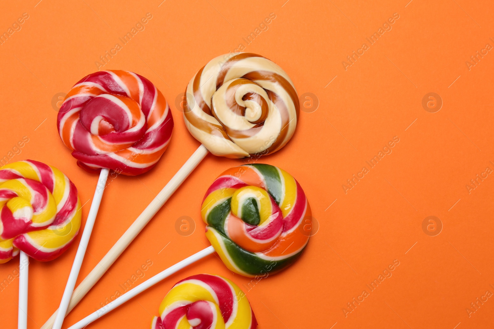 Photo of Sweet lollipops on orange background, flat lay. Space for text