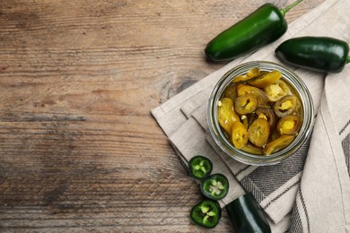 Photo of Fresh and pickled green jalapeno peppers on wooden table, flat lay. Space for text