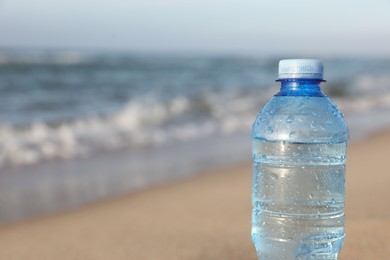 Plastic bottle of fresh water near sea, closeup. Space for text