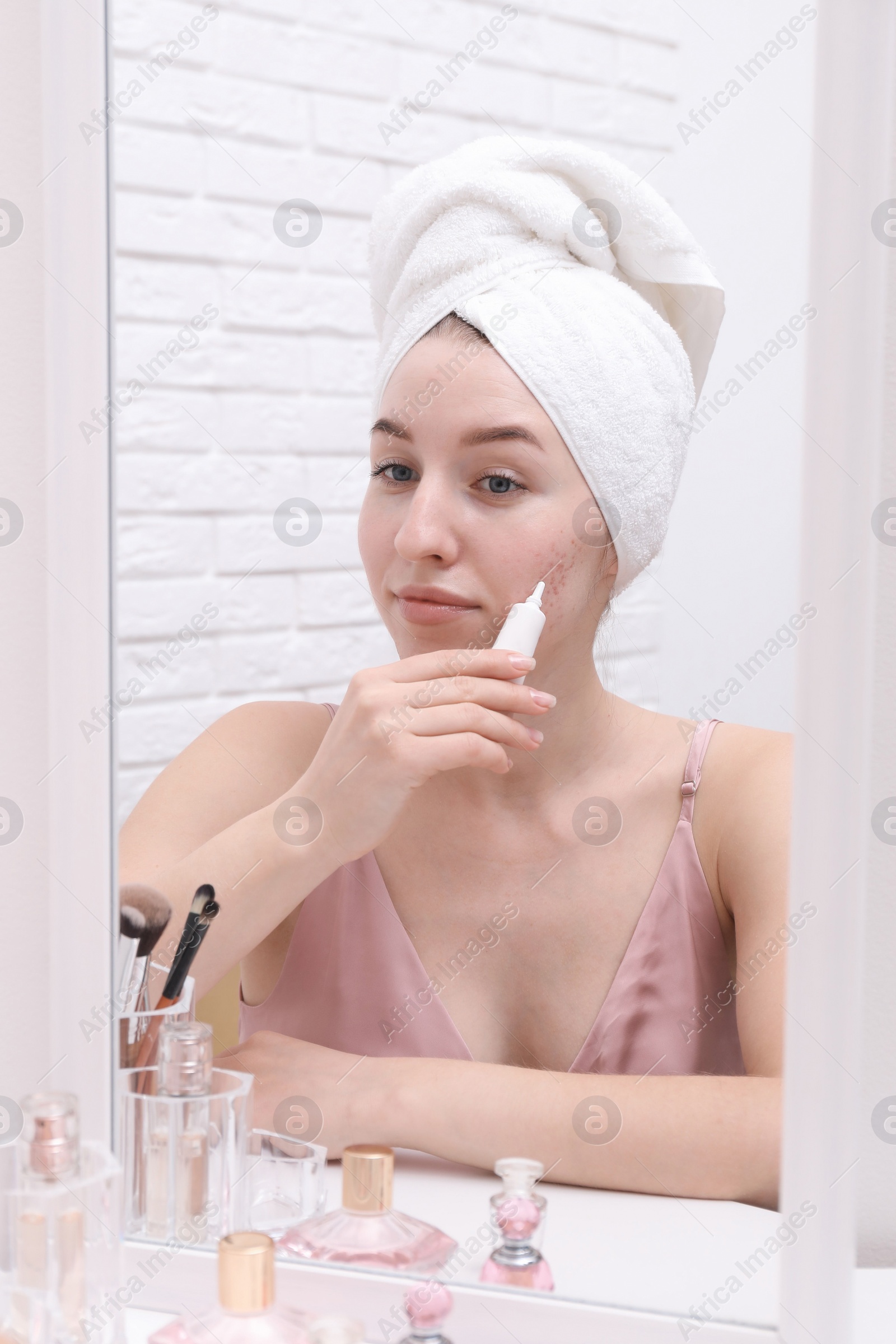 Photo of Woman with acne problem applying cream near mirror indoors