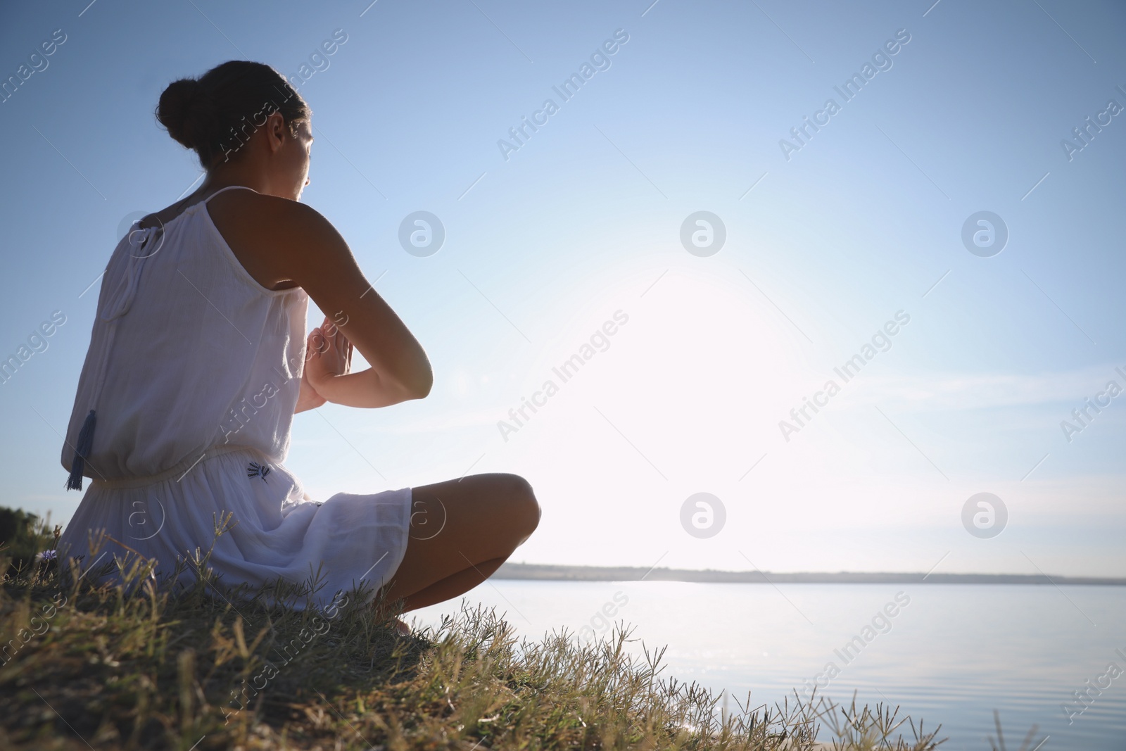 Photo of Young woman meditating near river at sunset, space for text. Nature healing power