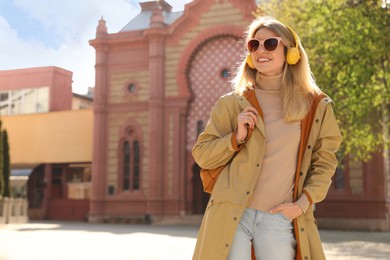 Happy young woman with headphones listening to music on city street