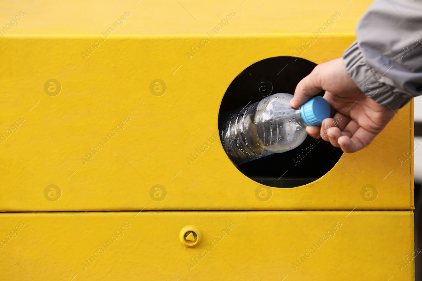 Photo of Man throwing plastic bottle into garbage bin outdoors, closeup. Waste sorting