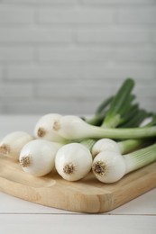 Photo of Fresh green spring onions on white wooden table. Space for text