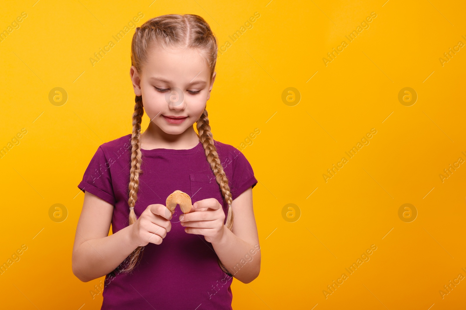 Photo of Cute girl holding tasty fortune cookie with prediction on orange background. Space for text