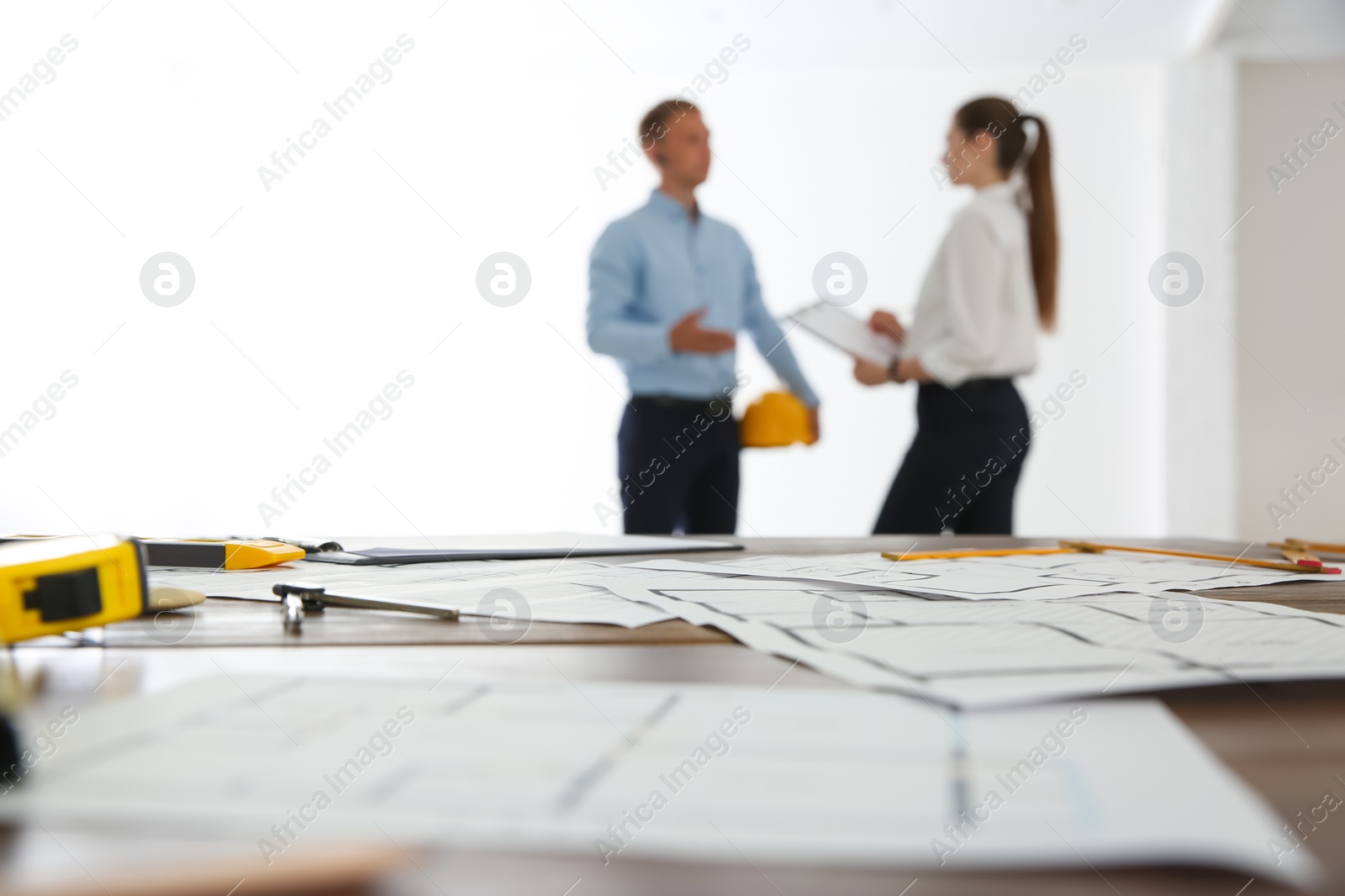 Photo of Colleagues in office, focus on table with construction drawings and tools