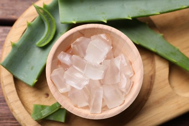 Aloe vera gel and slices of plant on wooden table, flat lay