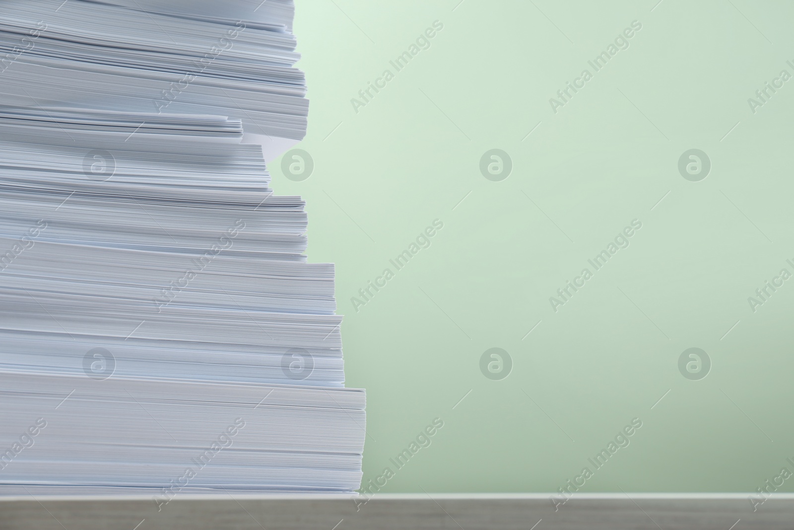 Photo of Stack of paper sheets on white table against light green background, closeup. Space for text