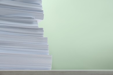 Stack of paper sheets on white table against light green background, closeup. Space for text