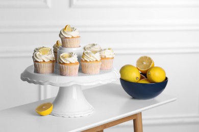 Photo of Delicious lemon cupcakes with cream and lemons in bowl on white table indoors