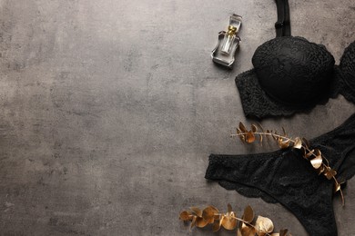 Elegant black women's underwear, perfume and decorative golden branches on gray textured background, flat lay. Space for text