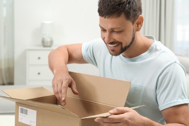 Photo of Happy man opening parcel at home. Internet shopping