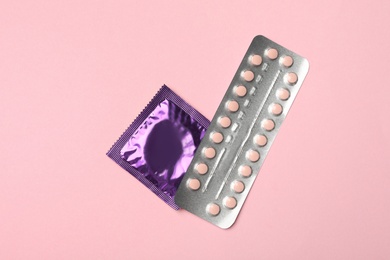 Photo of Condom and birth control pills on pink background, top view. Safe sex