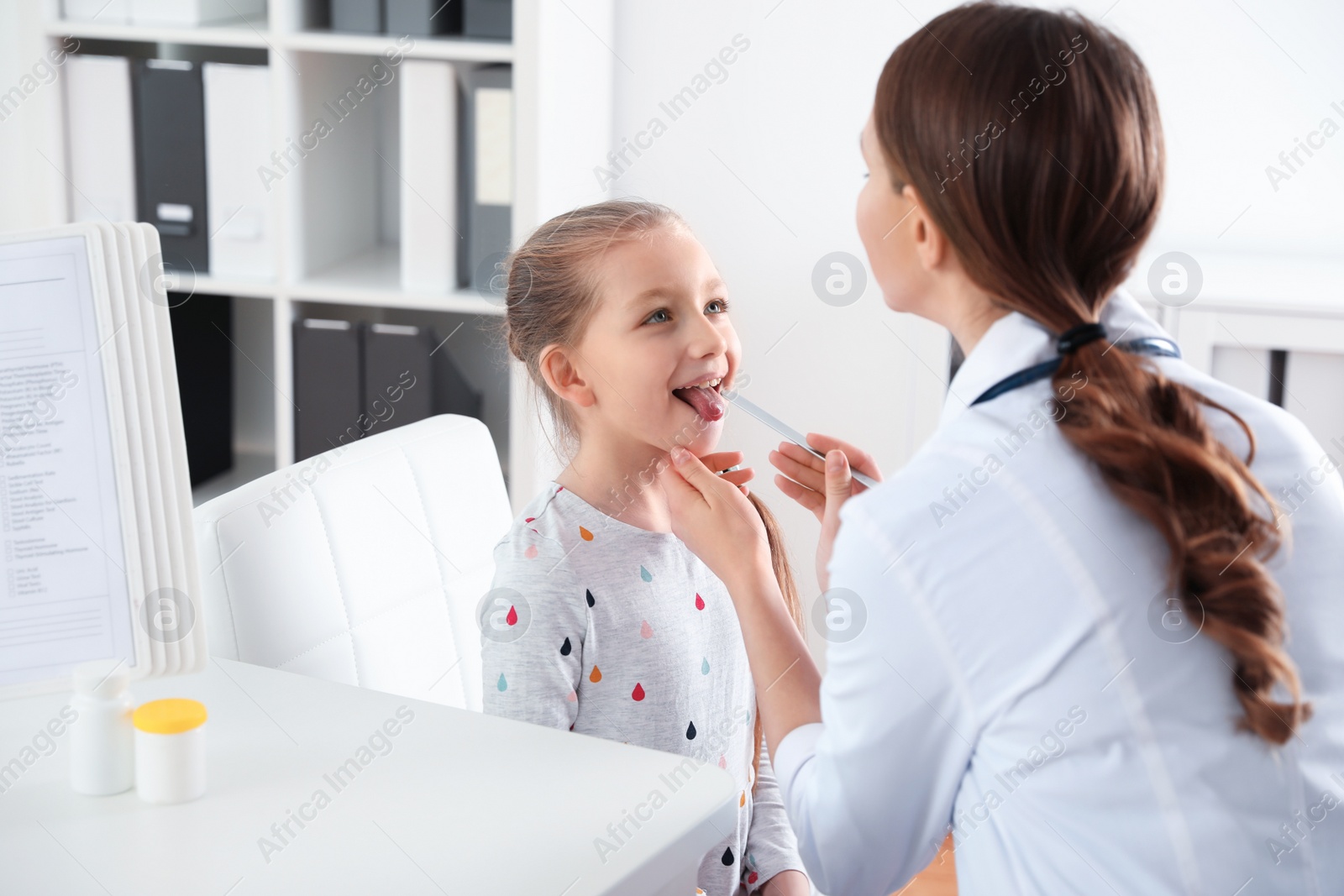 Photo of Children's doctor examining little patient's throat in clinic