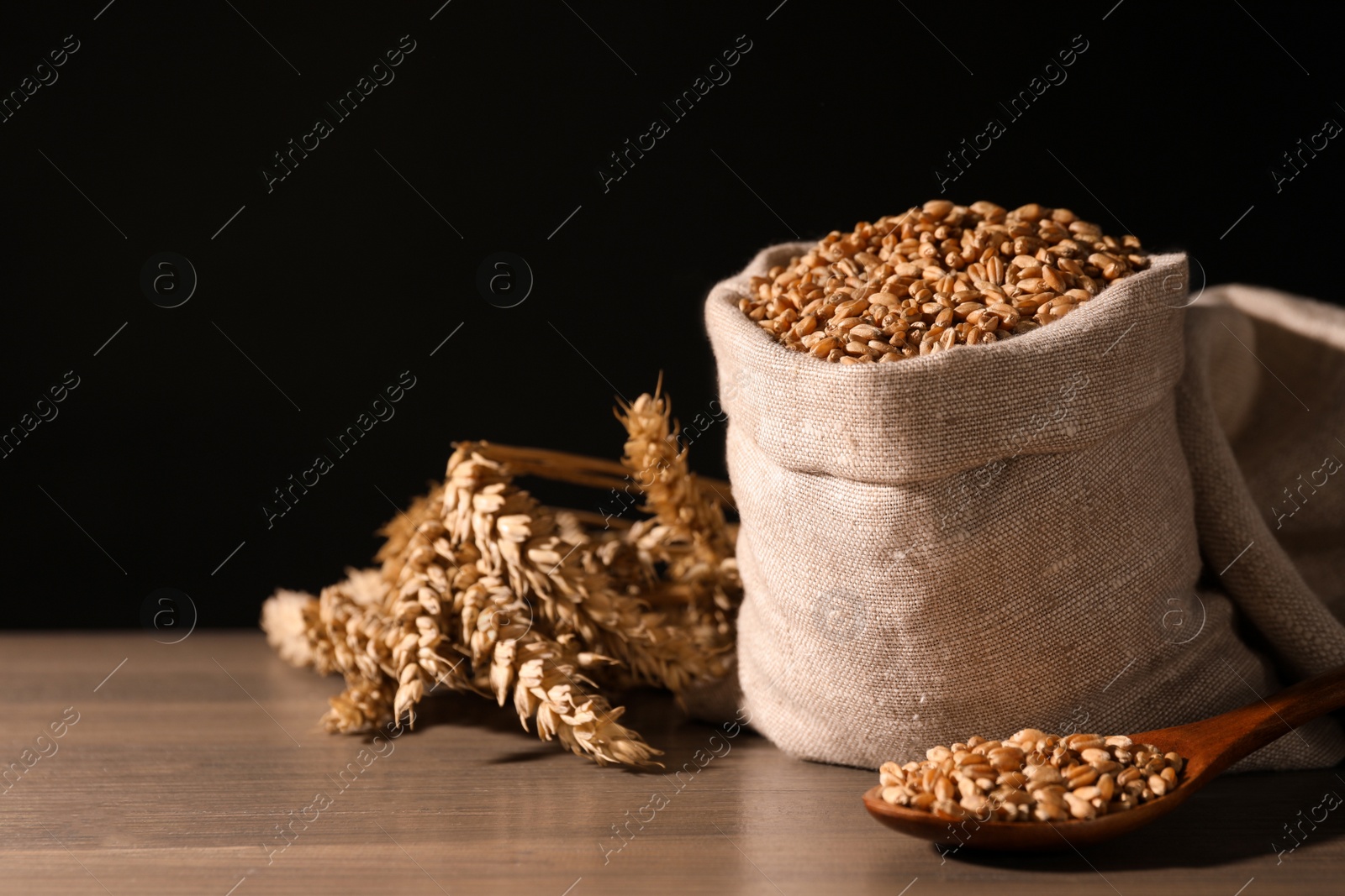 Photo of Wheat grains with spikelets on wooden table against black background, space for text