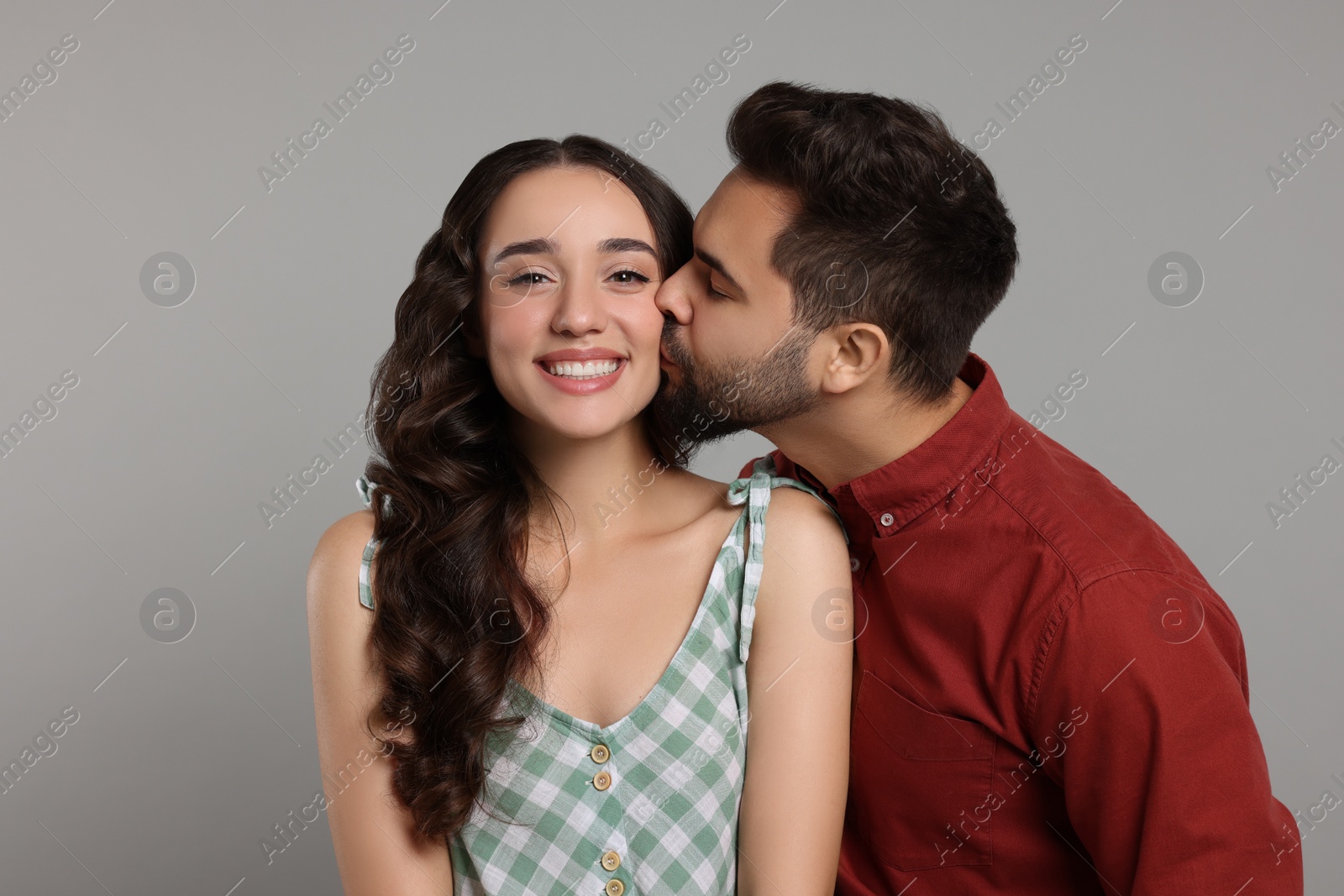 Photo of Man kissing his smiling girlfriend on grey background