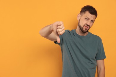 Man showing thumb down on orange background, space for text