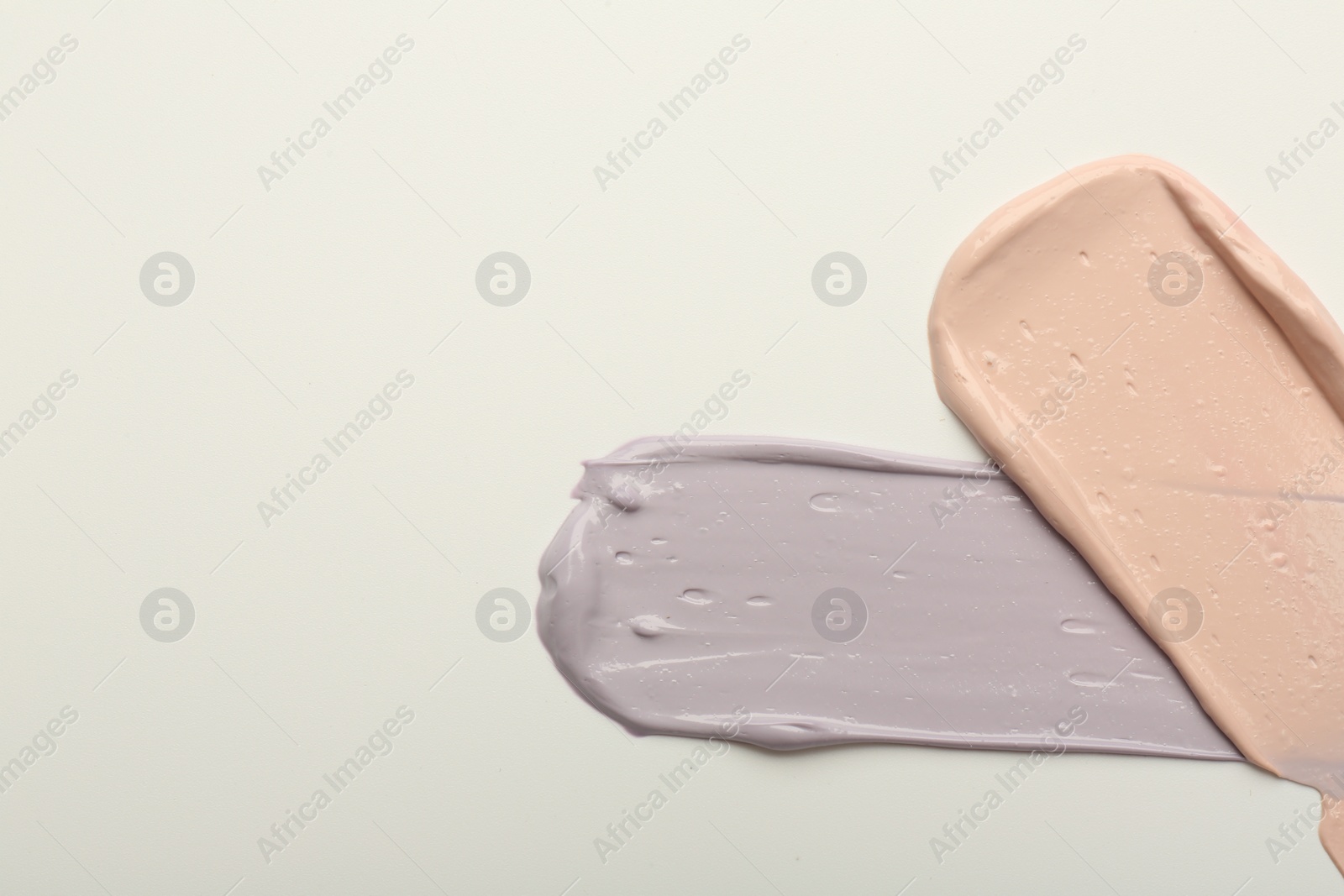 Photo of Strokes of pink and purple color correcting concealers on white background, top view