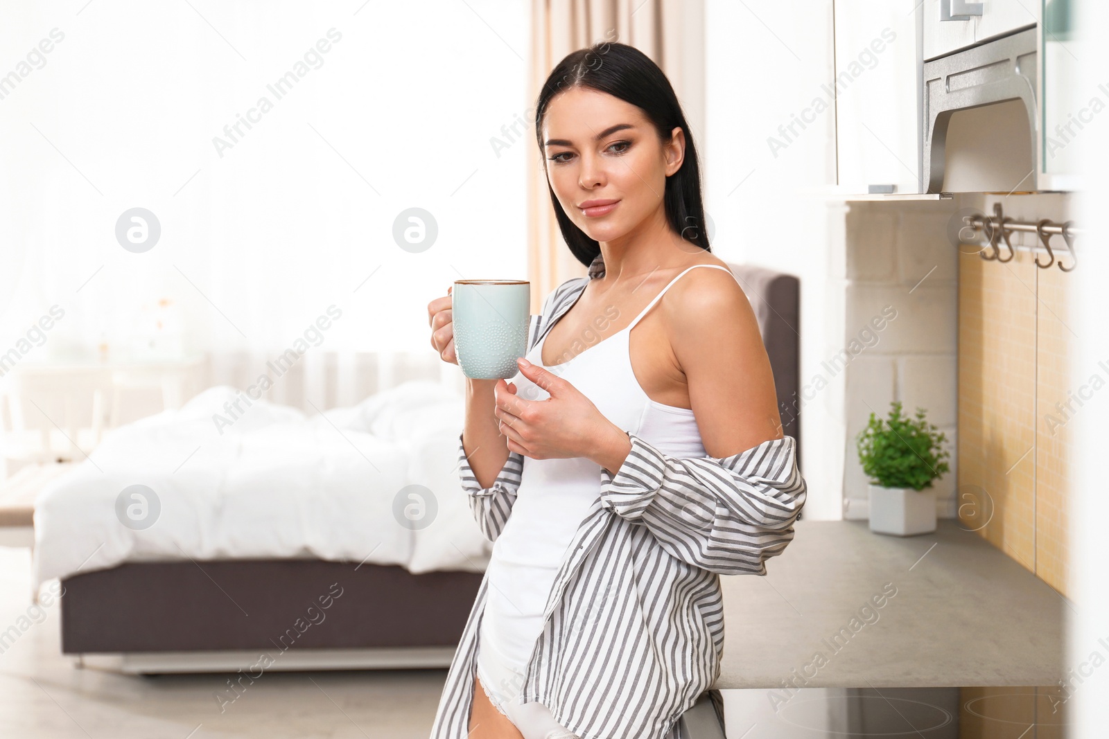 Photo of Beautiful young woman in white underwear drinking coffee at home