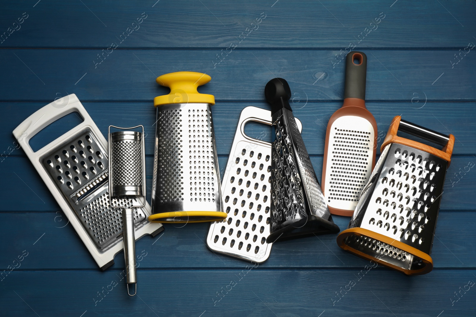 Photo of Different modern graters on blue wooden table, flat lay