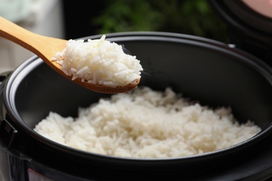 Spoon with tasty hot rice over cooker, closeup