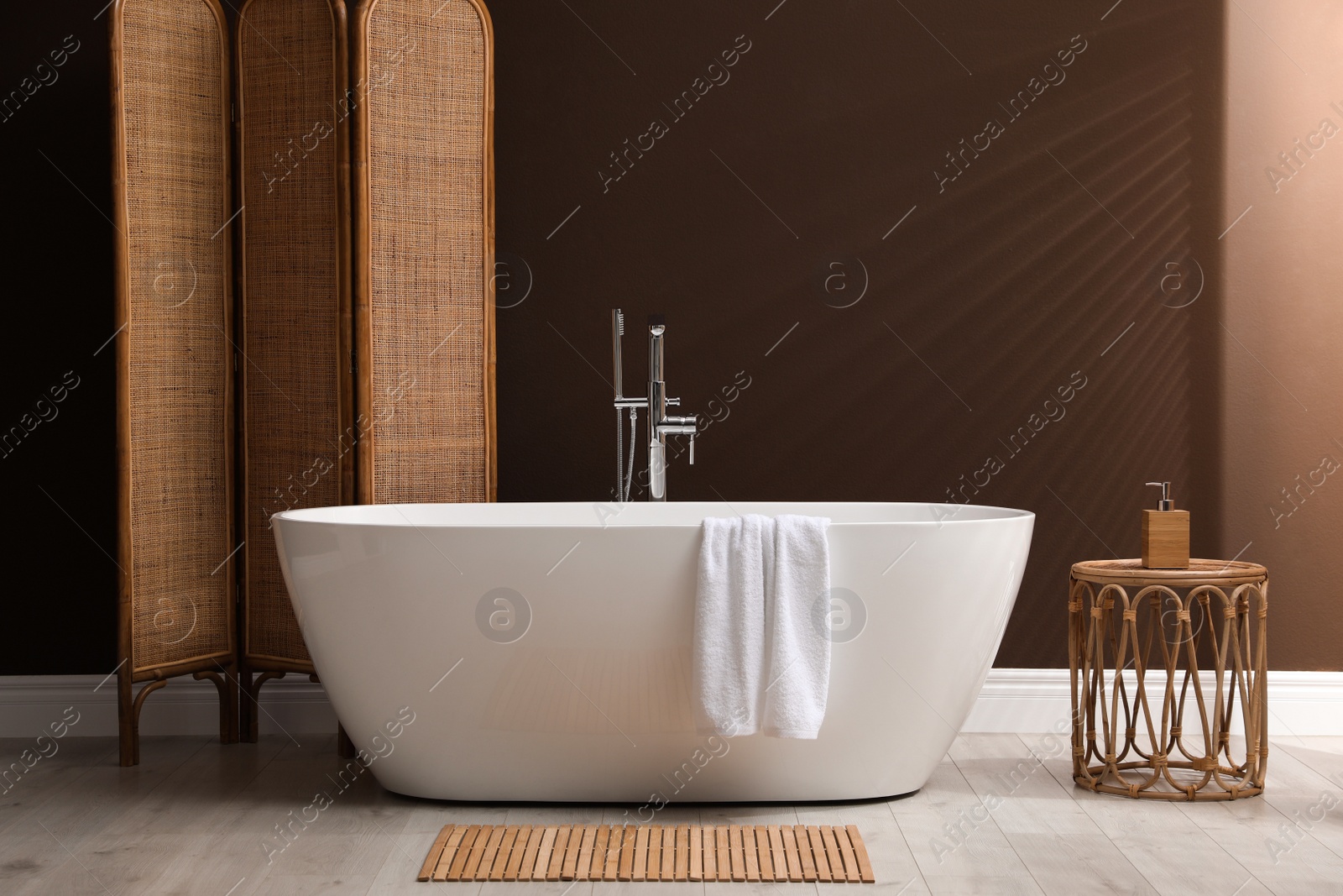 Photo of Modern ceramic bathtub and folding screen near brown wall in room