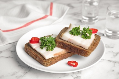 Plate with pork fatback sandwiches and shots of vodka on marble background