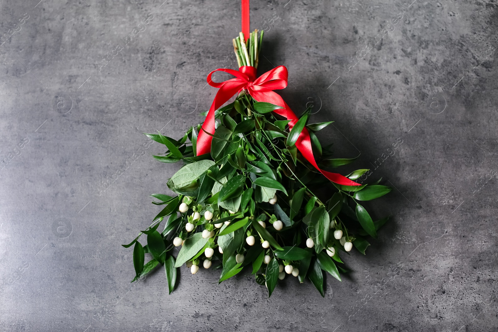 Photo of Mistletoe bunch with red bow hanging on grey wall. Traditional Christmas decor