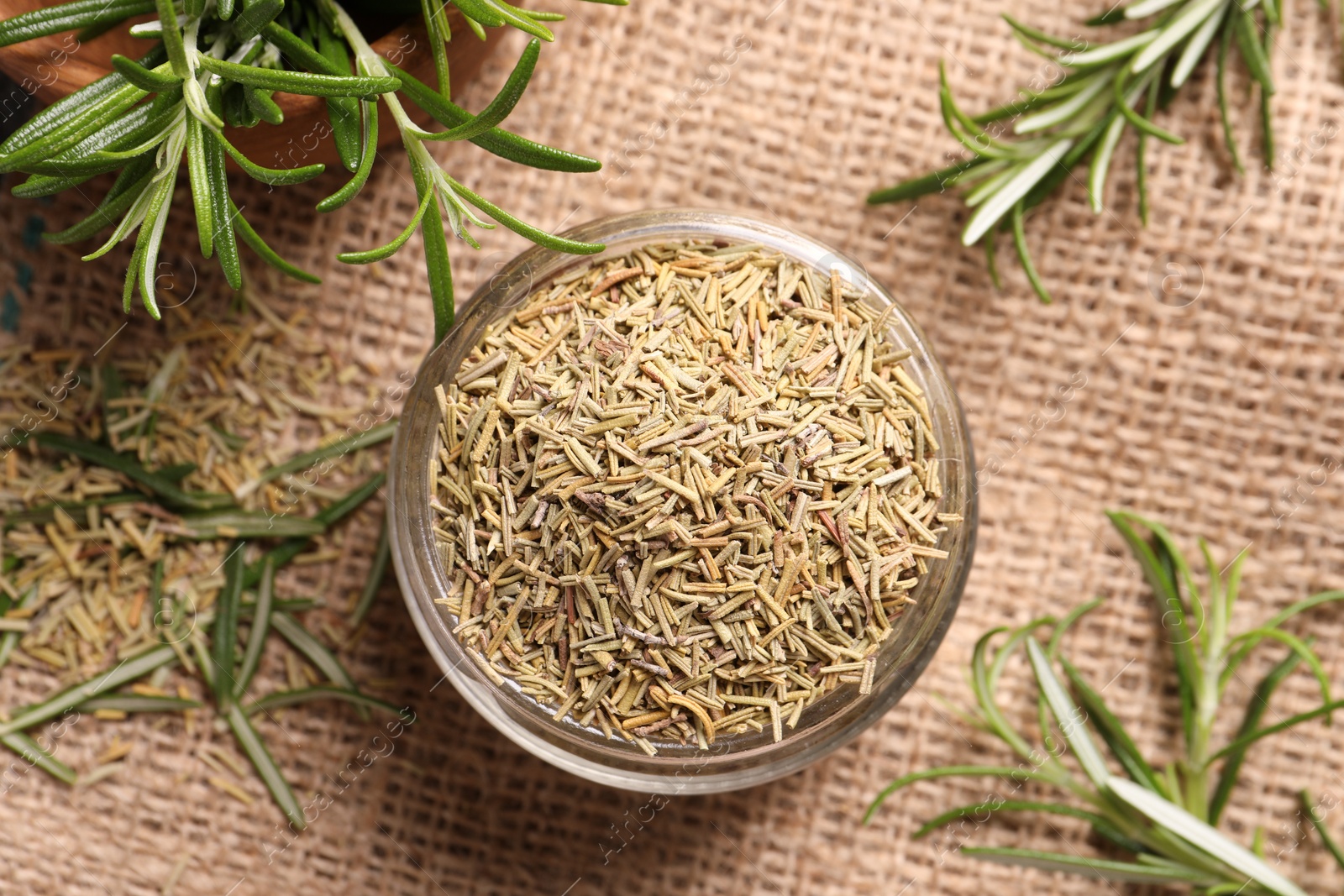 Photo of Dry and fresh rosemary on burlap fabric, flat lay