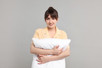 Photo of Happy woman in pyjama holding pillow on grey background